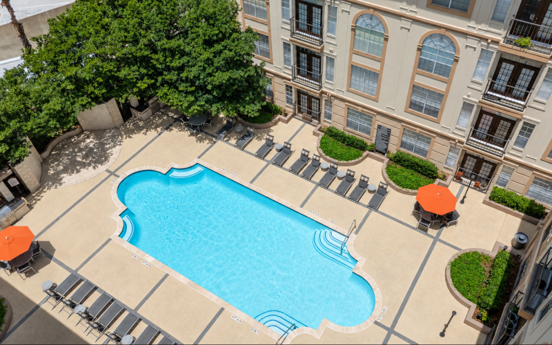 Resort-style swimming pool with lounge seating and apartment residences at Deerwood Apartments in Houston, Texas.