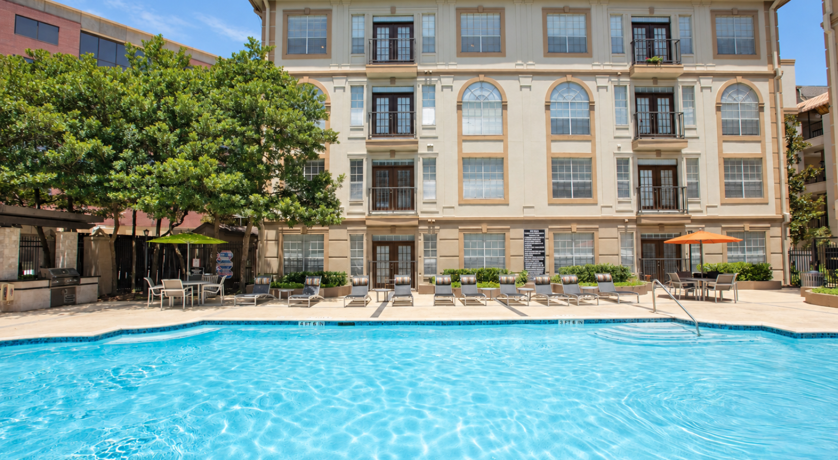 Resort-style swimming pool with lounge seating and apartment residences at Deerwood Apartments in Houston, Texas.